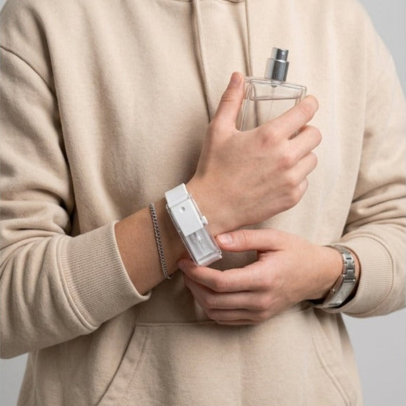 Man refilling Baswick white perfume bracelet from a fragrance bottle, wearing beige hoodie.
